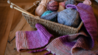 basket of yarn, knitting needles and a knitted scarf